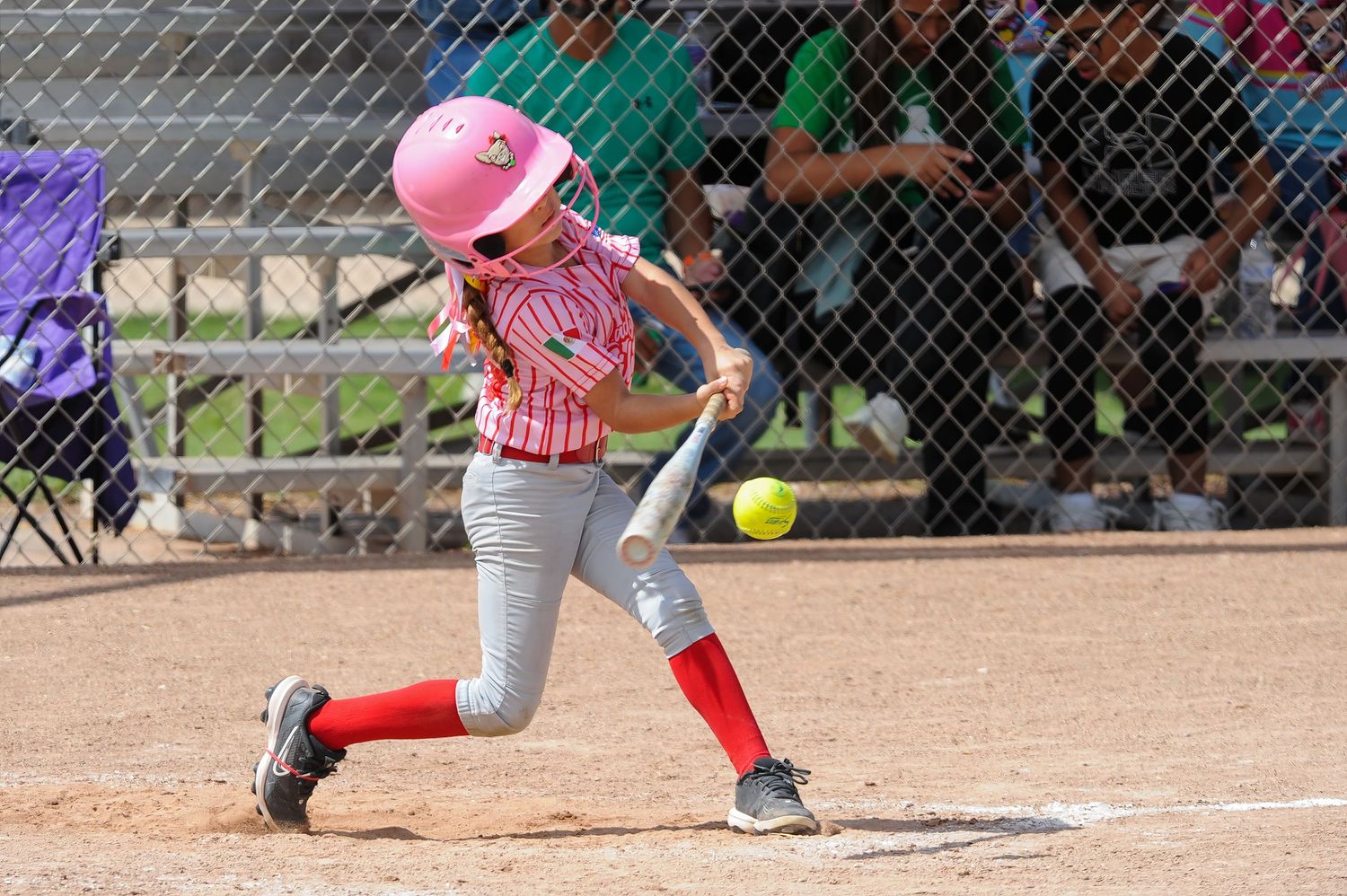 Young softball player in pink helmet swings at a yellow ball during a youth league game.