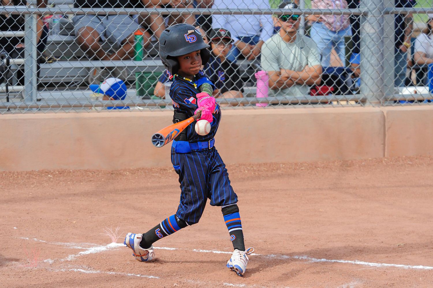 Young girl softball player in navy uniform connecting with pitch during competitive youth softball game.