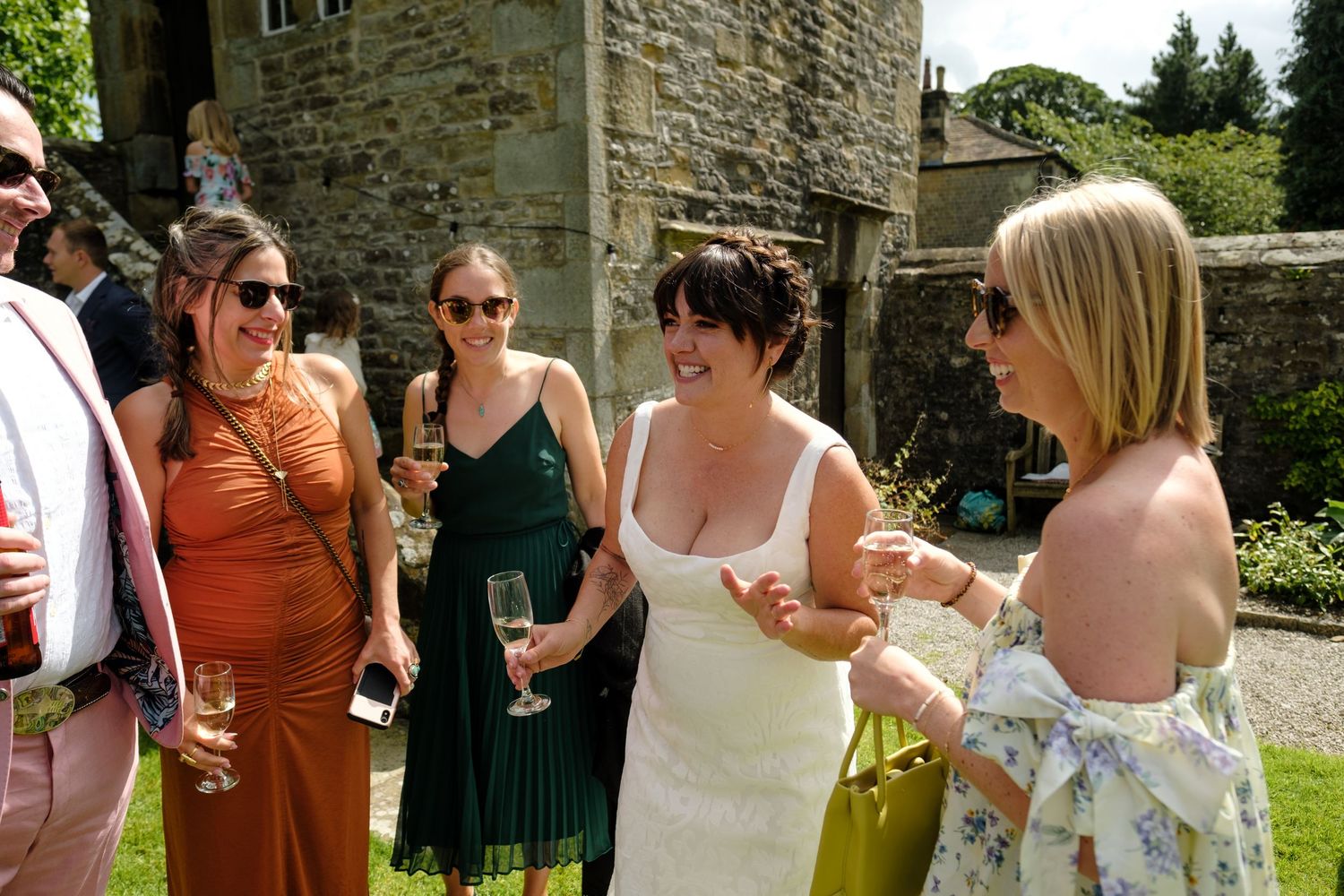 Wedding guests socialize in front of a rustic stone building wall. Norfolk and Norwich wedding photographer.