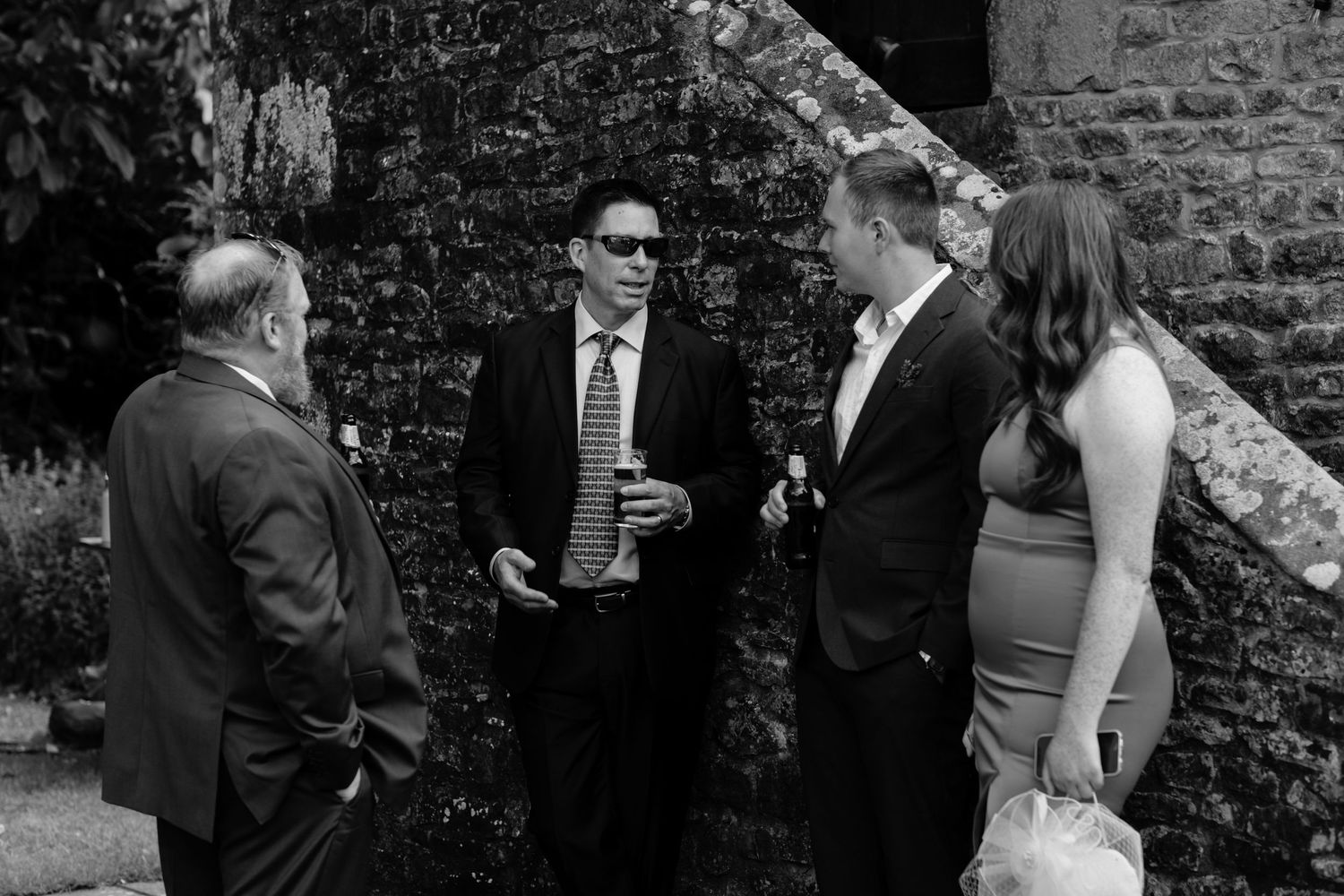 Wedding guests mingling and enjoying cocktails against a stone wall backdrop at an outdoor reception. Norfolk and Norwich wedding photograph