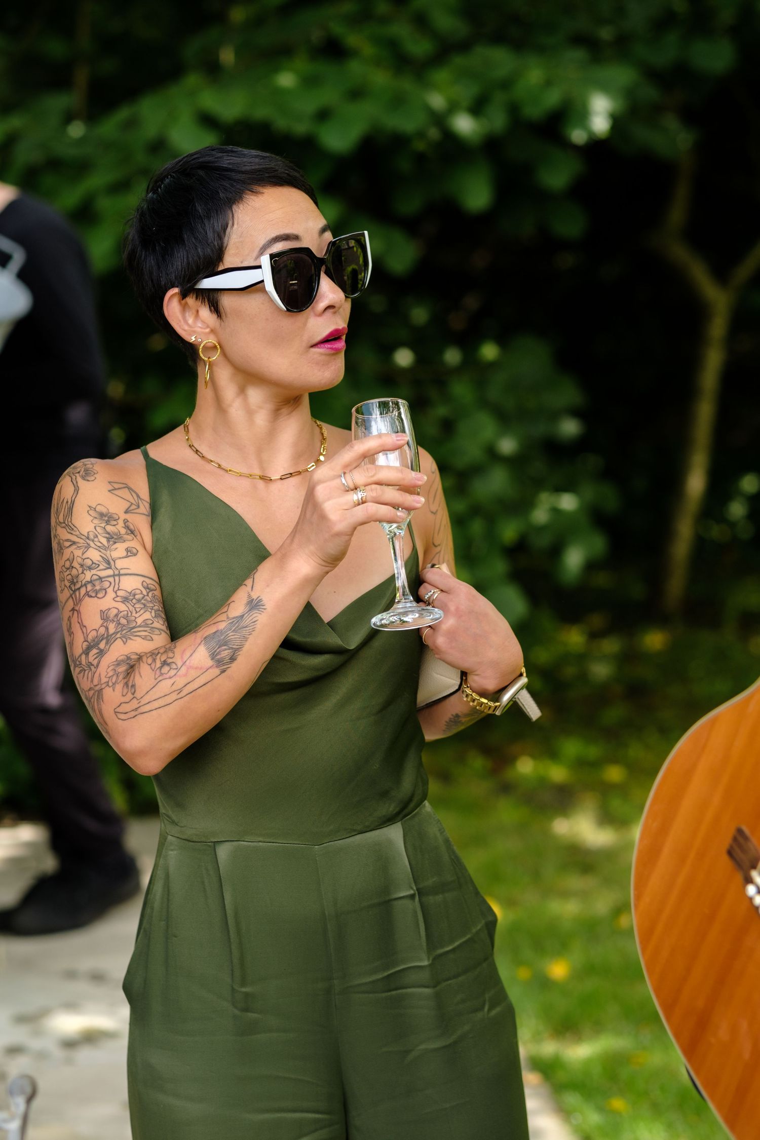 Guest in olive green dress enjoying champagne at outdoor wedding reception. Norfolk and Norwich wedding photographer.