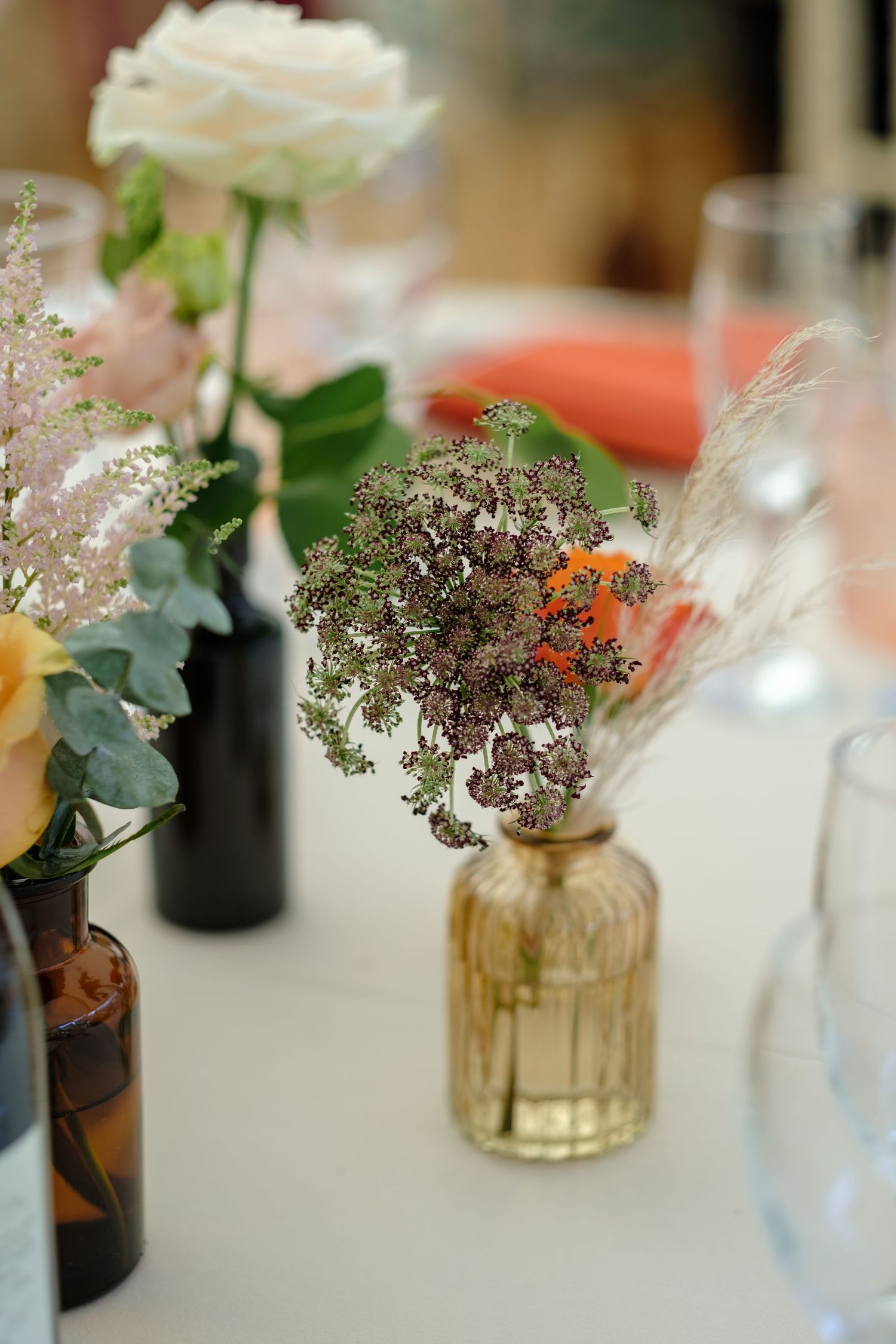 Vintage-style flower arrangements in mixed glass vases at wedding reception. Norfolk and Norwich wedding photographer.
