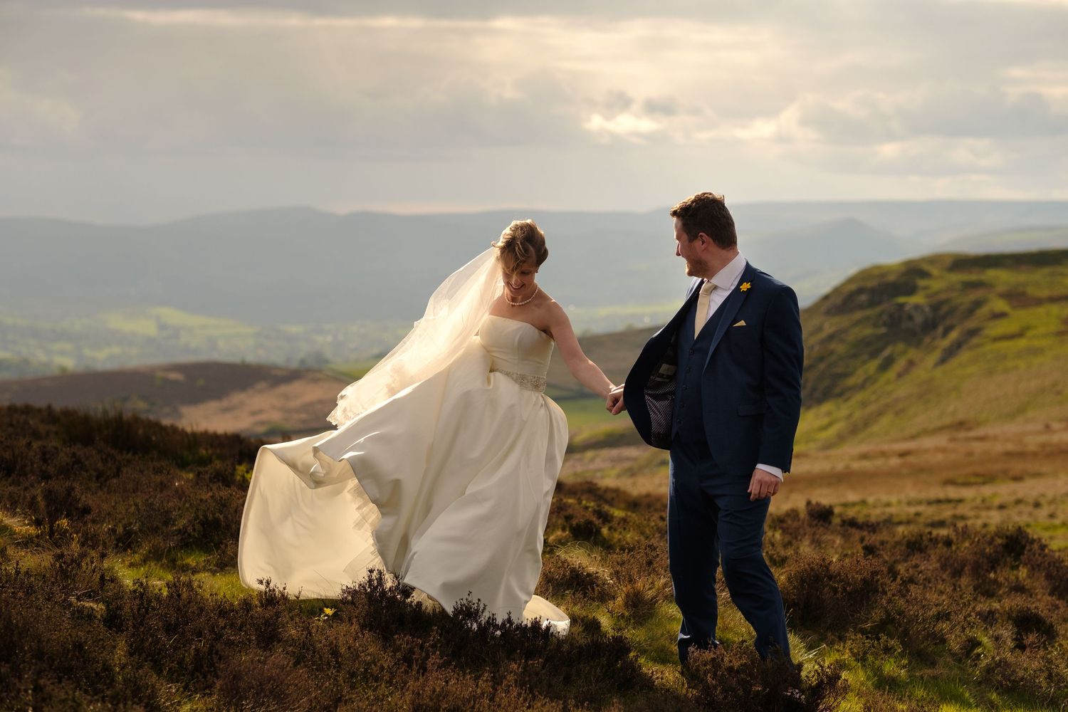 Wedding couple walks along rolling hills and moorland under moody skies - by Norfolk Wedding Photographer.