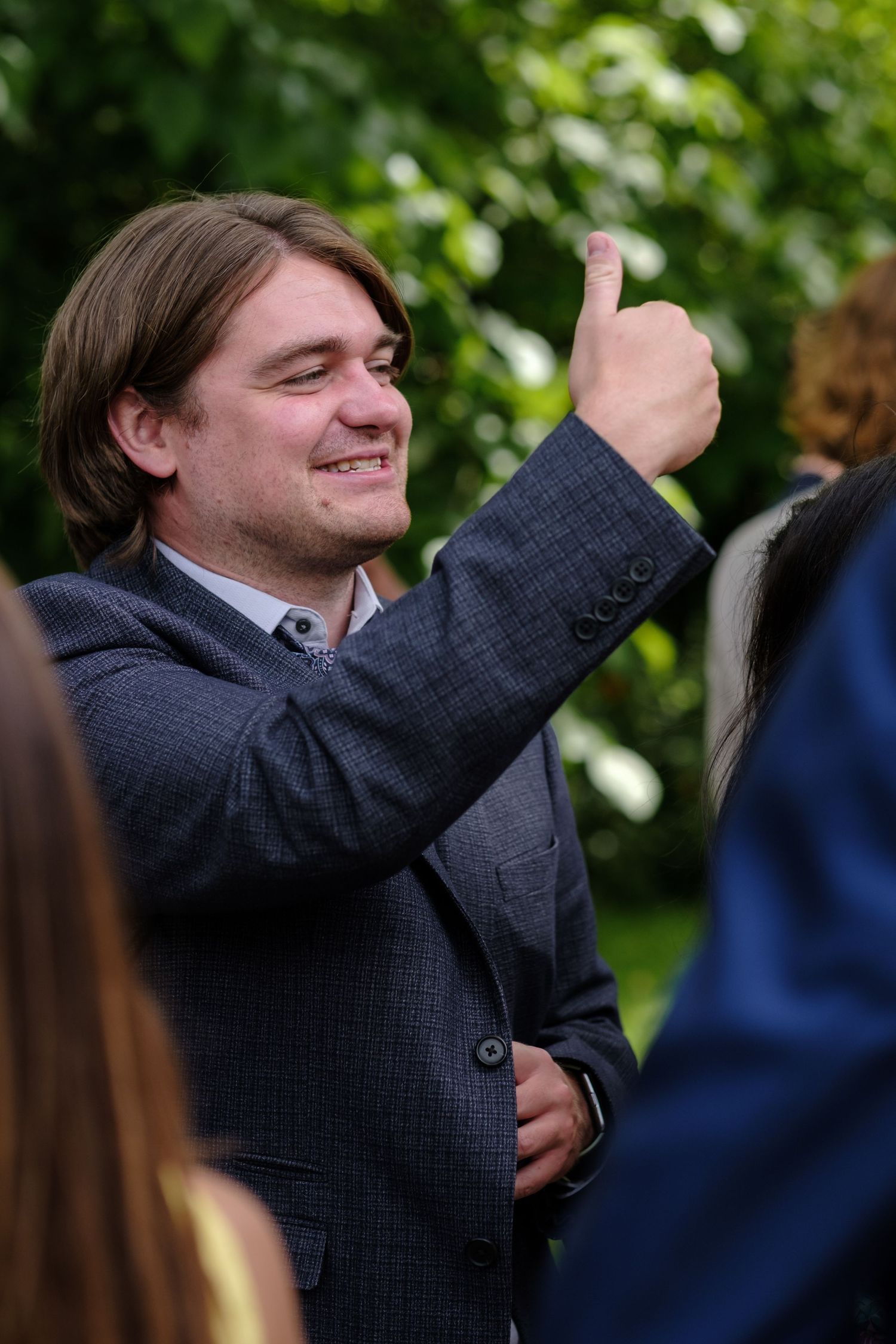 Person in a navy suit jacket gestures enthusiastically during an outdoor event. Norfolk and Norwich wedding photographer.