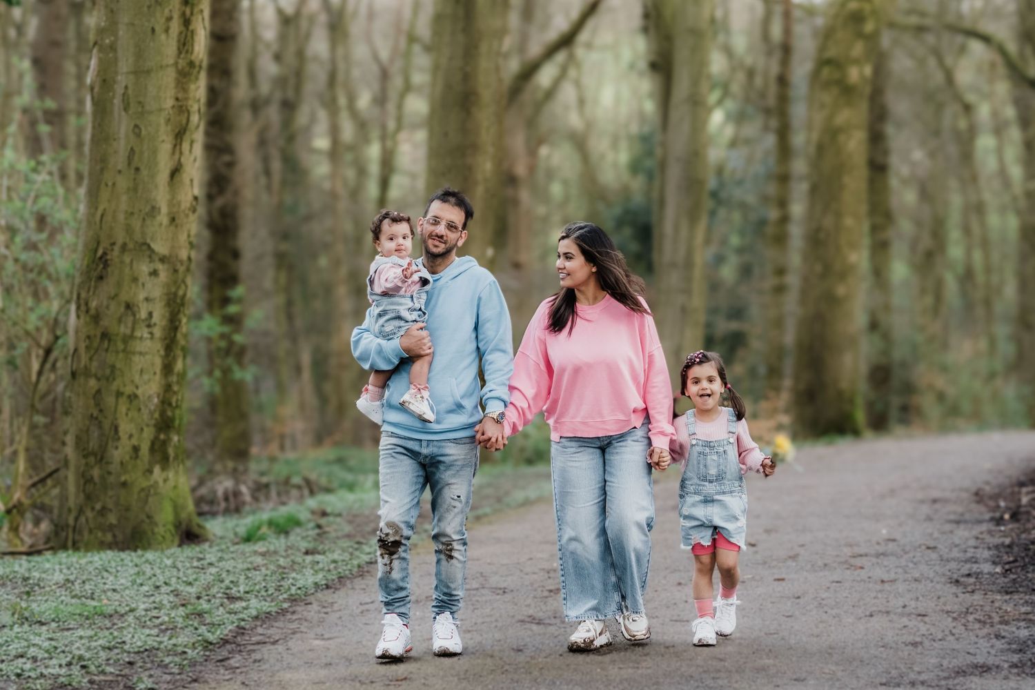 Family walking together on a peaceful forest trail wearing coordinated denim and pink outfits in spring.
