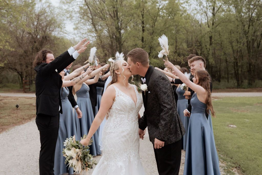 Bride and groom share a kiss during wedding party portraits at a rustic Rocky Meadow Farm wedding in Oklahoma with wedding party
