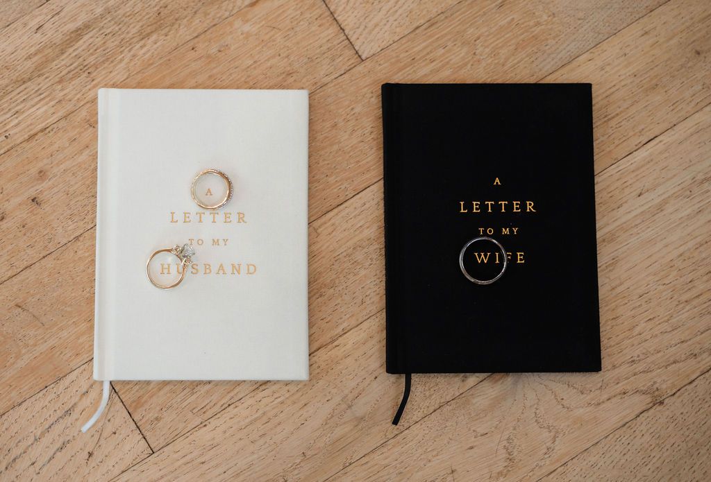 Two wedding journals, a white Letter to My Husband and black Letter to My Wife, with gold rings.