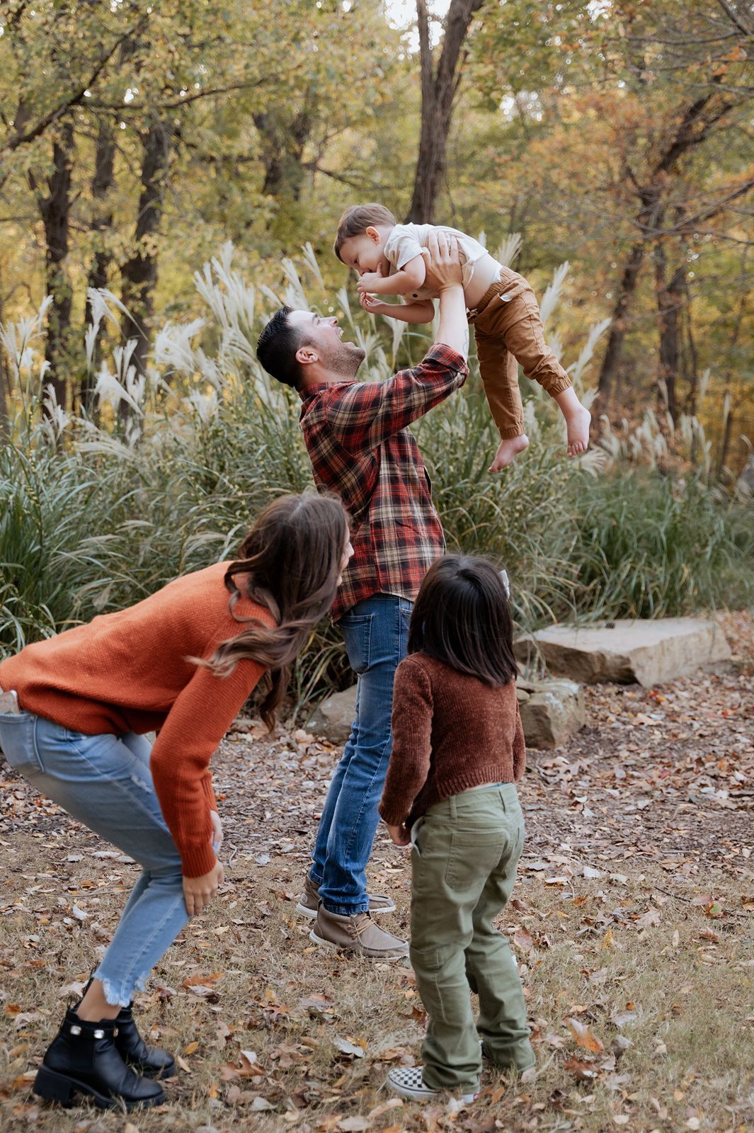 Playful Tulsa family photography session with dad lifting toddler while family laughs together in autumn park