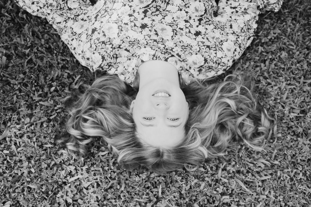 Aerial black and white portrait of young woman with long wavy hair lying in grass.