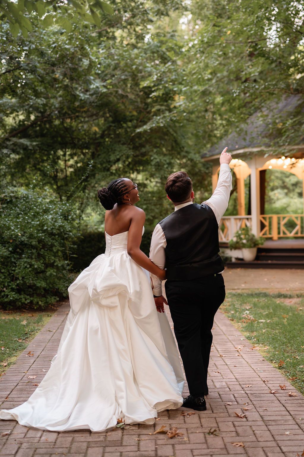 Bride and groom walk hand in hand down a brick path toward a garden venue.