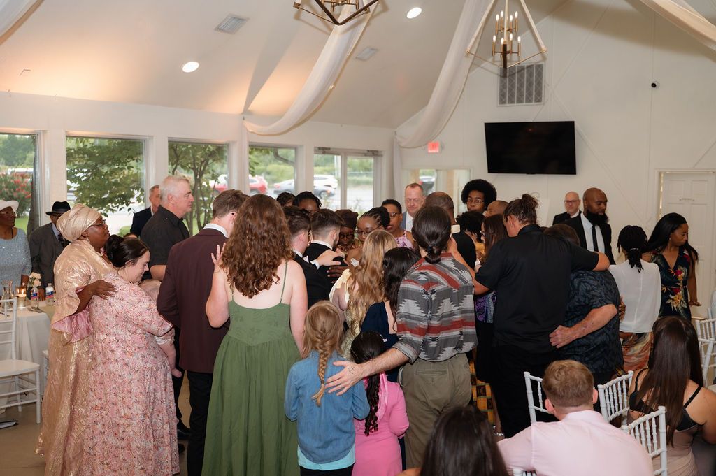Wedding reception guests gathered together in elegant white venue with vaulted ceilings and chandelier.