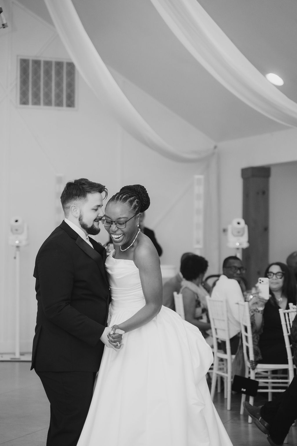 Black and white photo of a bride and groom sharing their first dance at a wedding reception.