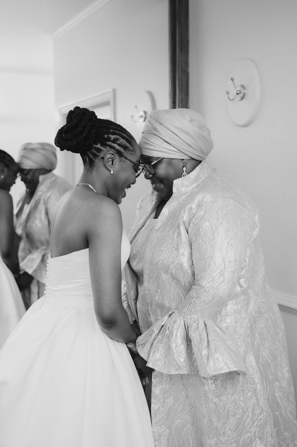 Black and white photo of a bride in a white gown sharing a tender forehead touch moment with her mother.