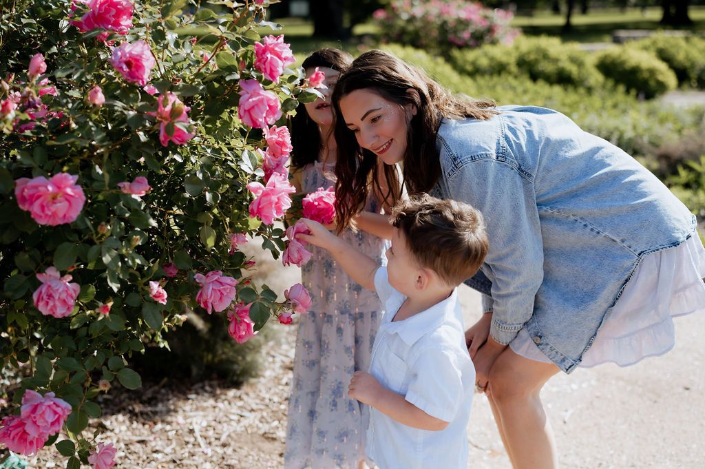 Mother & two children exploring pink roses during a candid motherhood photography session at Woodward Park in Tulsa, Oklahoma.