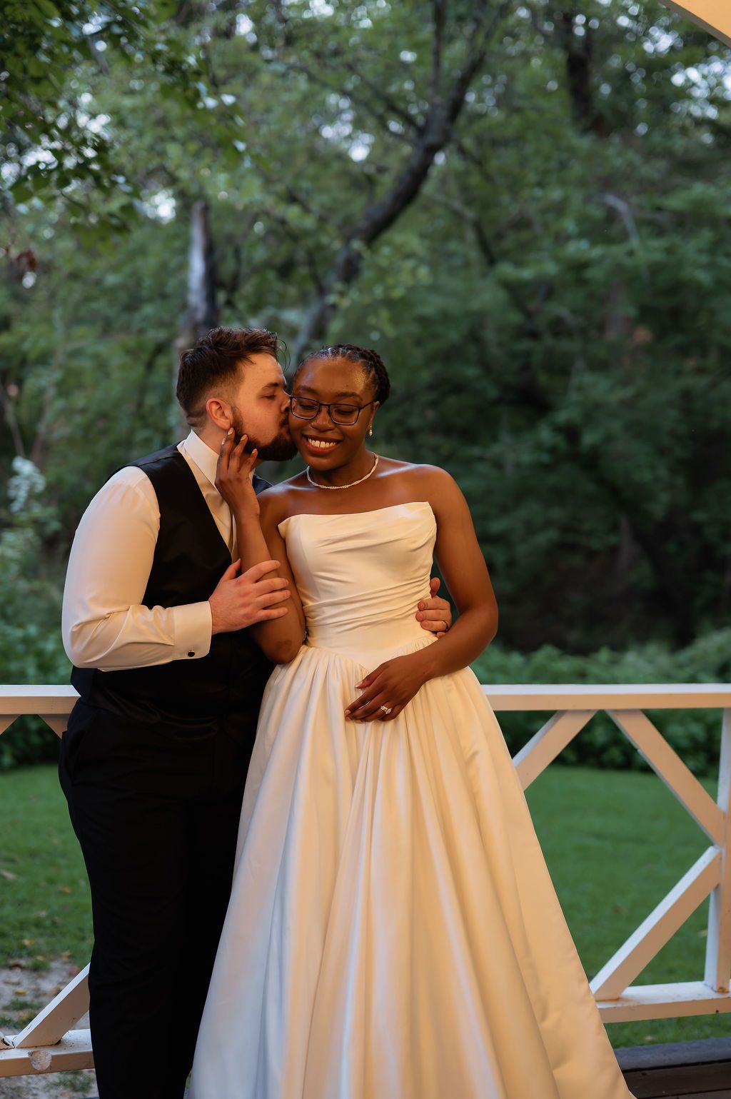 Groom whispers in brides ear as she smiles on a decorated outdoor wedding deck.