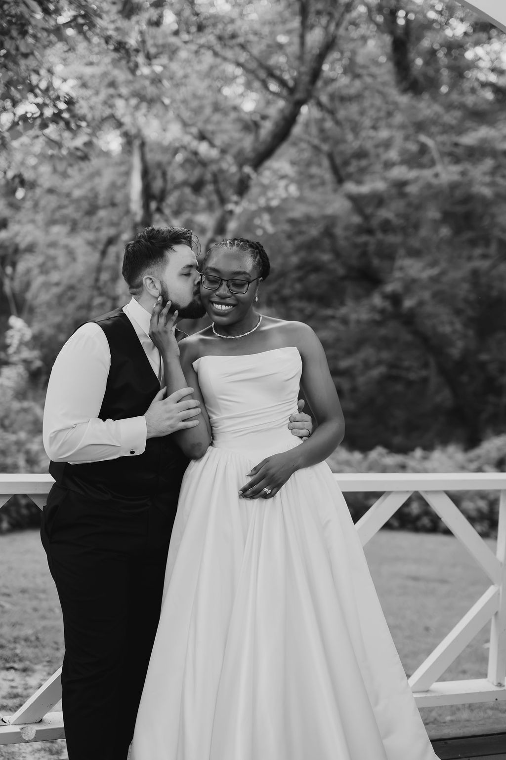 Black and white photo of groom whispering to smiling bride on an outdoor wedding deck.