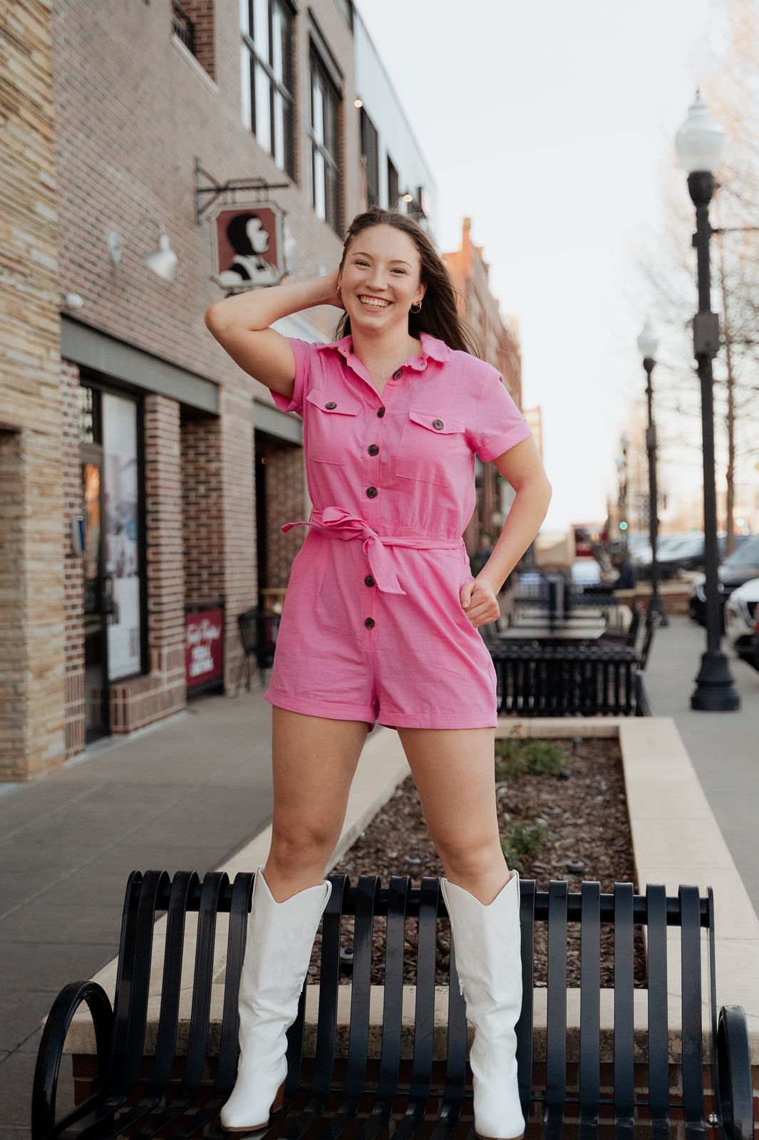 Girl standing on a bench with one hand in her pocket and the other fixing her hair for the camera