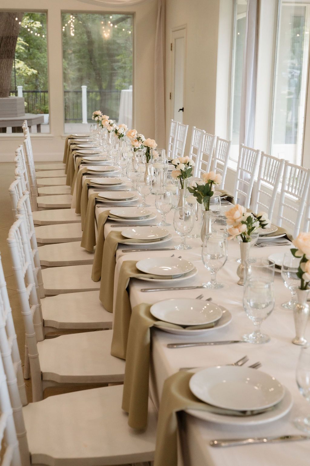 Elegant wedding reception table with white chiavari chairs, neutral linens, white plates, crystal glasses, and blush floral centerpieces.