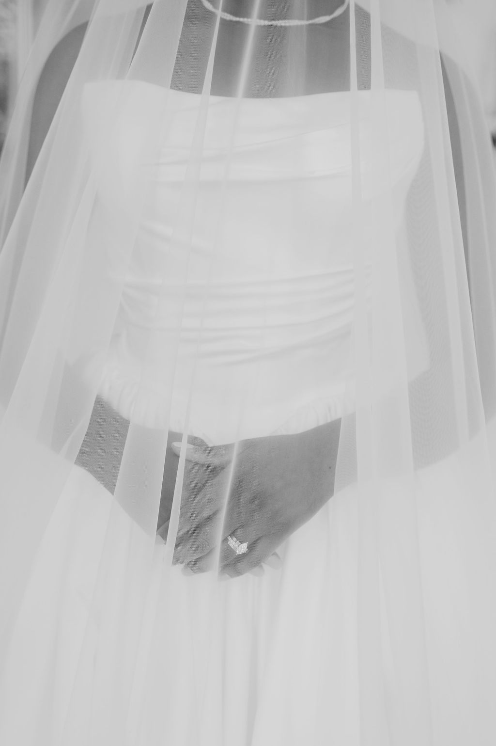 Close-up black and white photo of bride in strapless gown with veil and diamond engagement ring on her hand.
