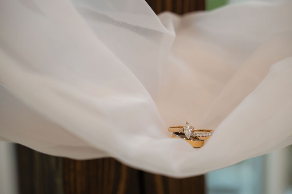Gold marquise diamond engagement ring and wedding band resting on flowing white bridal veil fabric.