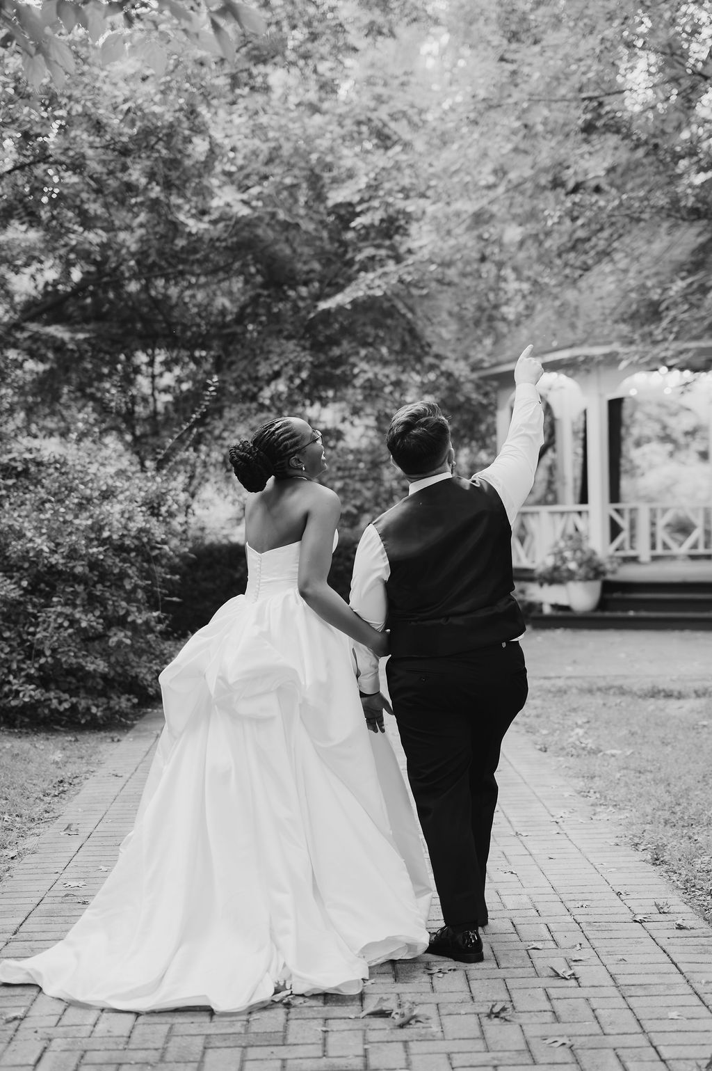 Black and white photo of newlywed couple walking hand in hand on brick path, bride in ball gown, groom in suit.