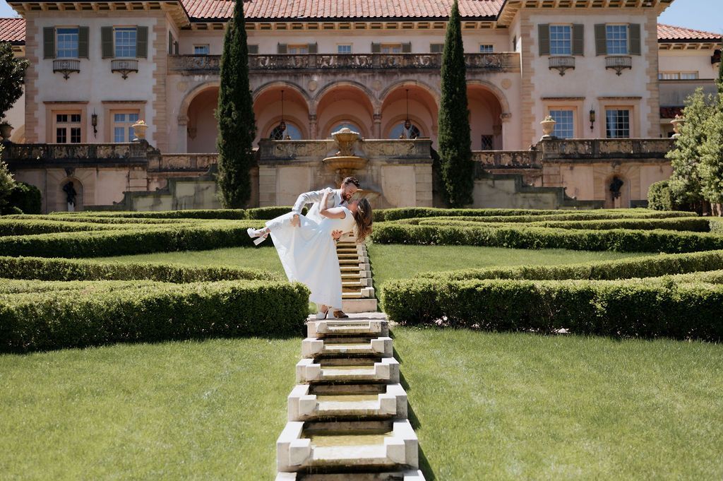 Couple doing a dip and kiss in Philbrook formal gardens for engagement photos with tulsa wedding photographer