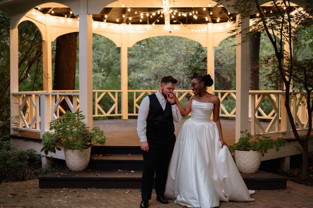 Bride and groom laughing together in front of a lit gazebo at an outdoor wedding venue.
