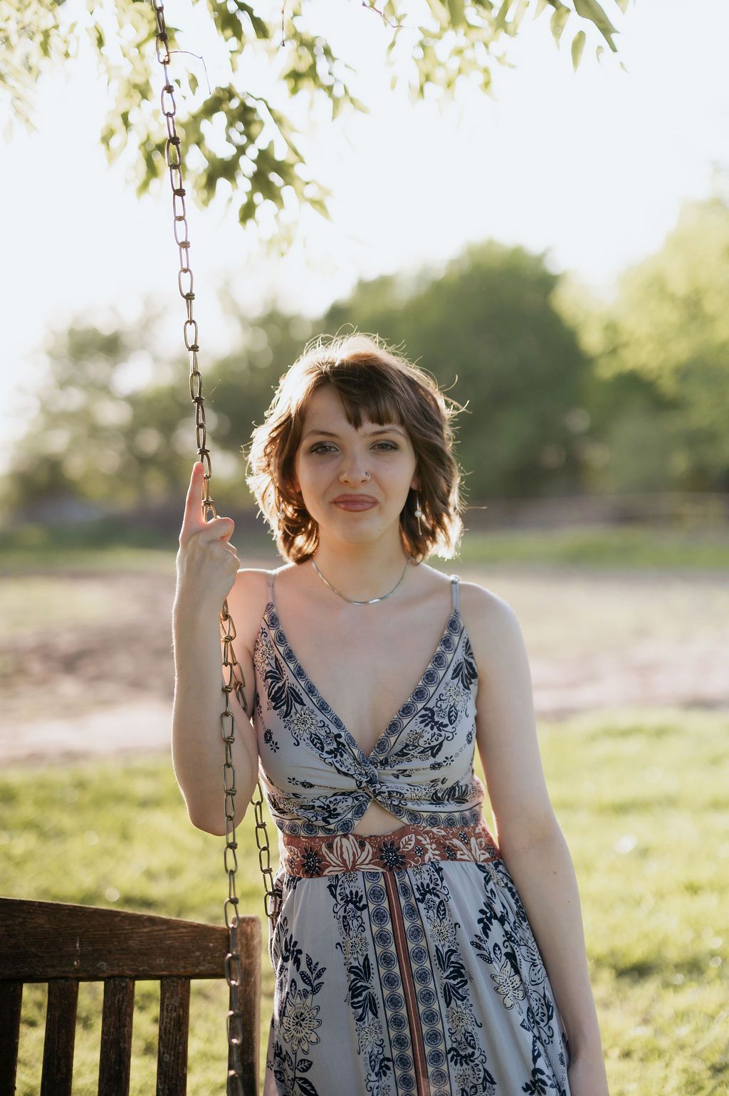 Young woman in floral sundress holding swing chain in sunny field