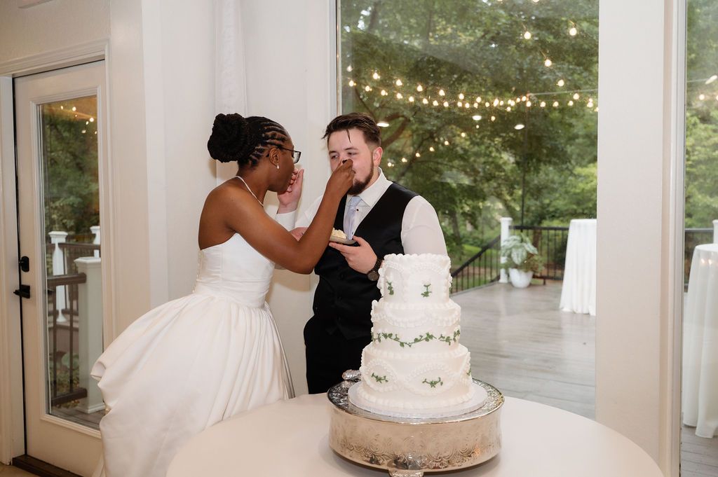 Bride playfully smashes wedding cake on grooms face during cake cutting ceremony.