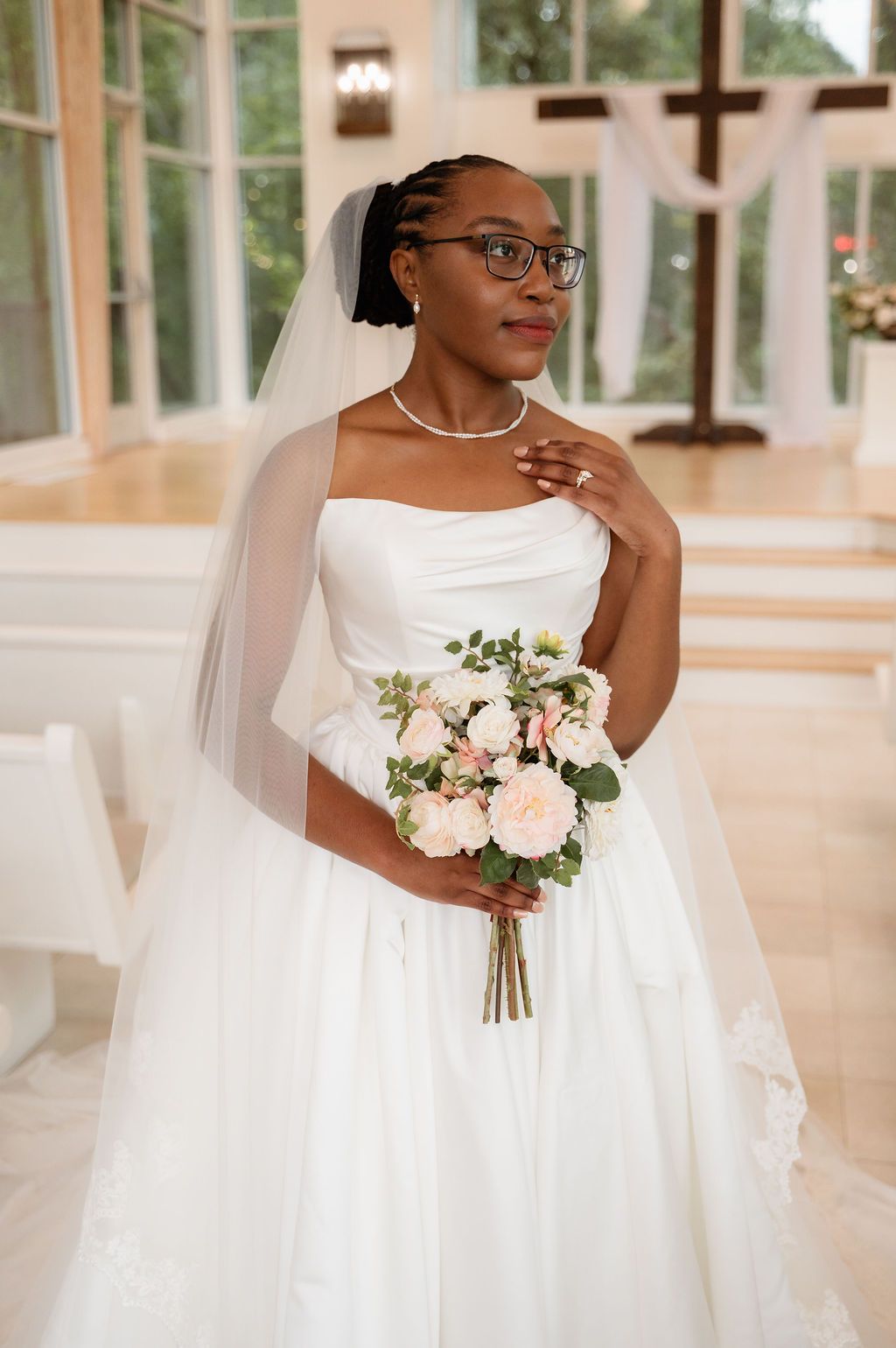 Elegant Black bride in strapless white gown and veil holds blush bouquet inside chapel.