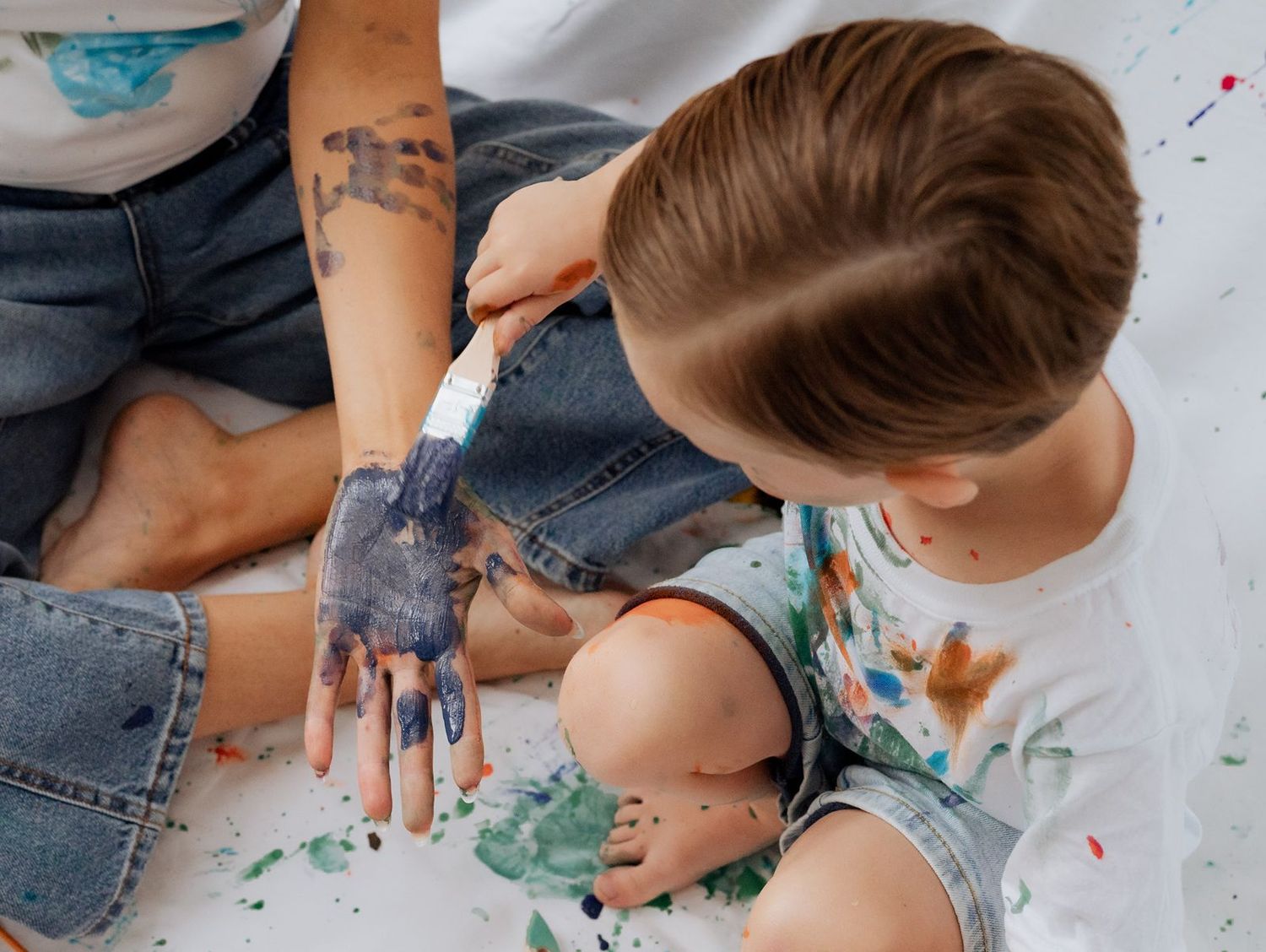 Son painting mom's hand in a park