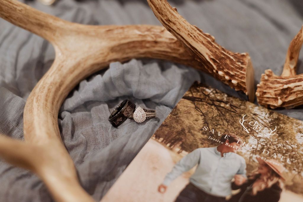Diamond engagement ring resting against rustic deer antlers on blue fabric- detail shot for Oklahoma rustic wedding
