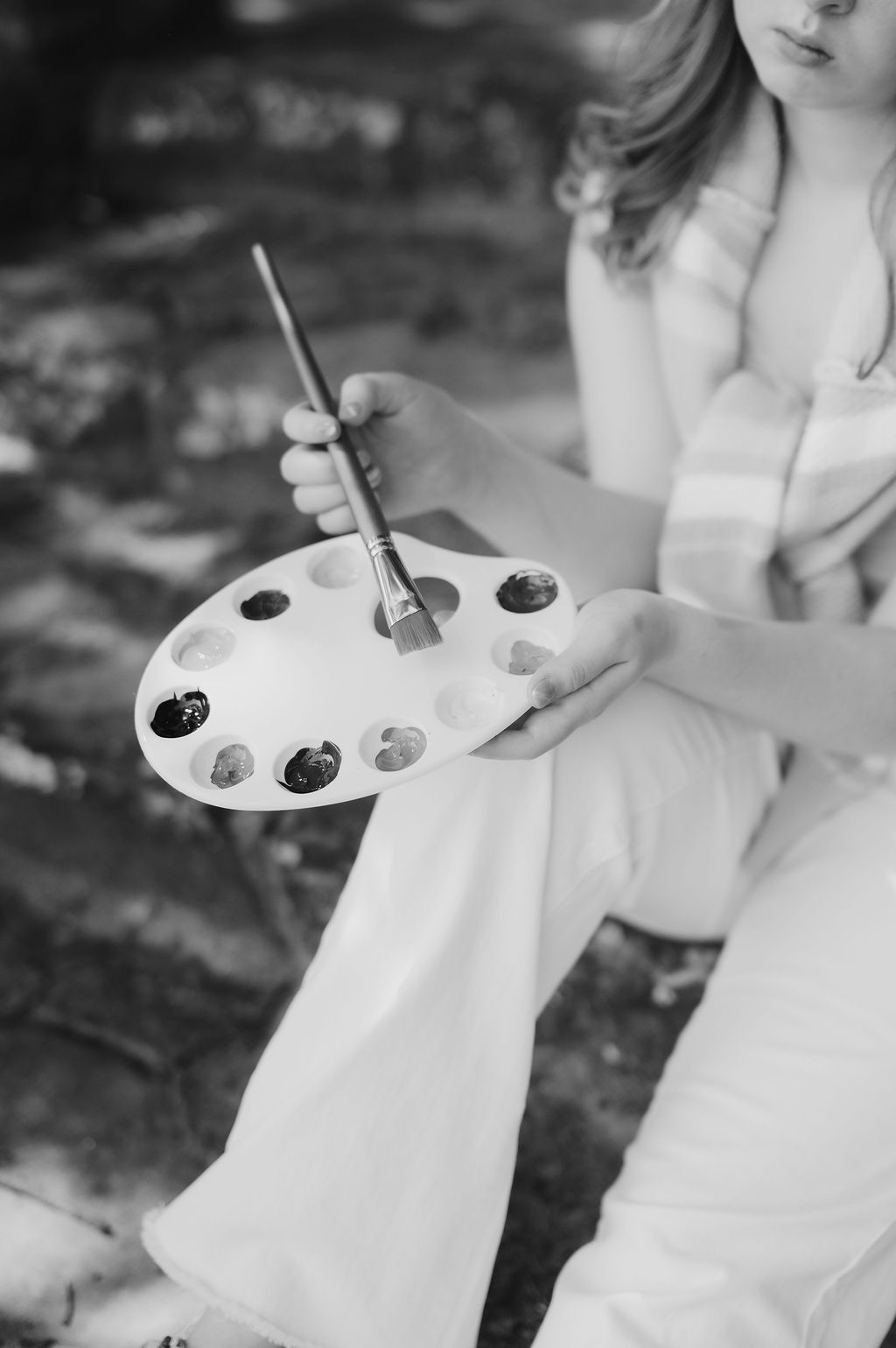 Black and white close-up of hands holding a paint palette and brush while seated outdoors at Tulsa's Woodward Park
