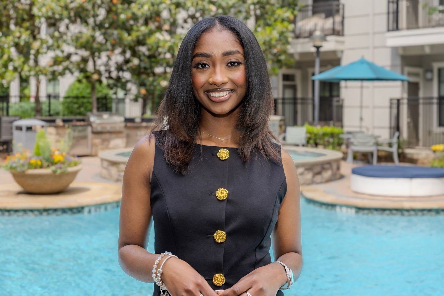 Professional outdoor portrait by a pool wearing a navy dress with gold buttons.