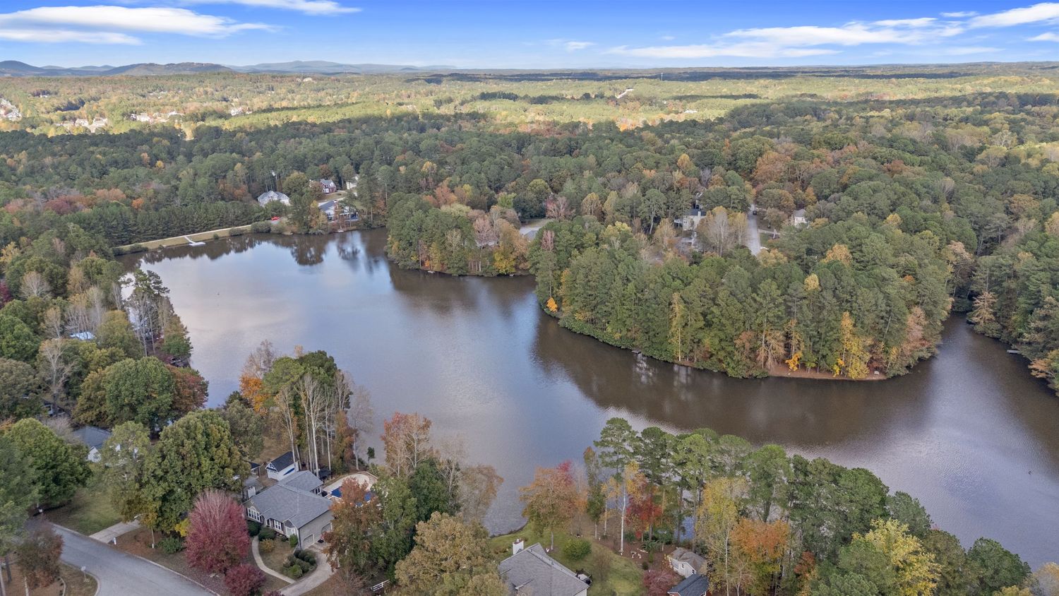 Panoramic aerial view of a winding lake surrounded by colorful autumn trees and forest landscapes.