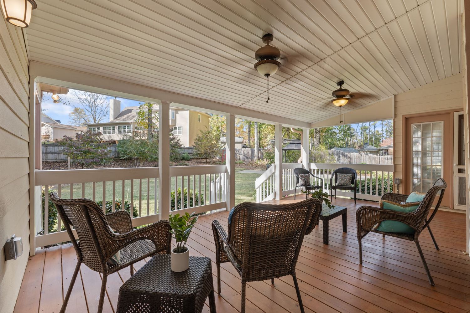 Cozy screened porch with wicker furniture and ceiling fans overlooking a backyard garden setting.