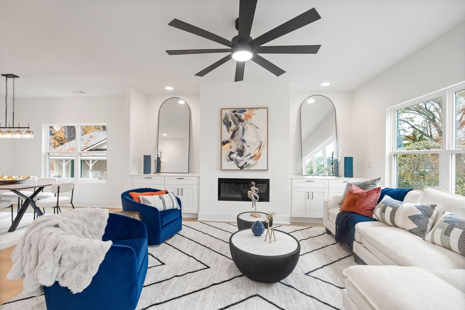 Modern white living room interior design with blue accent furniture and ceiling fan.