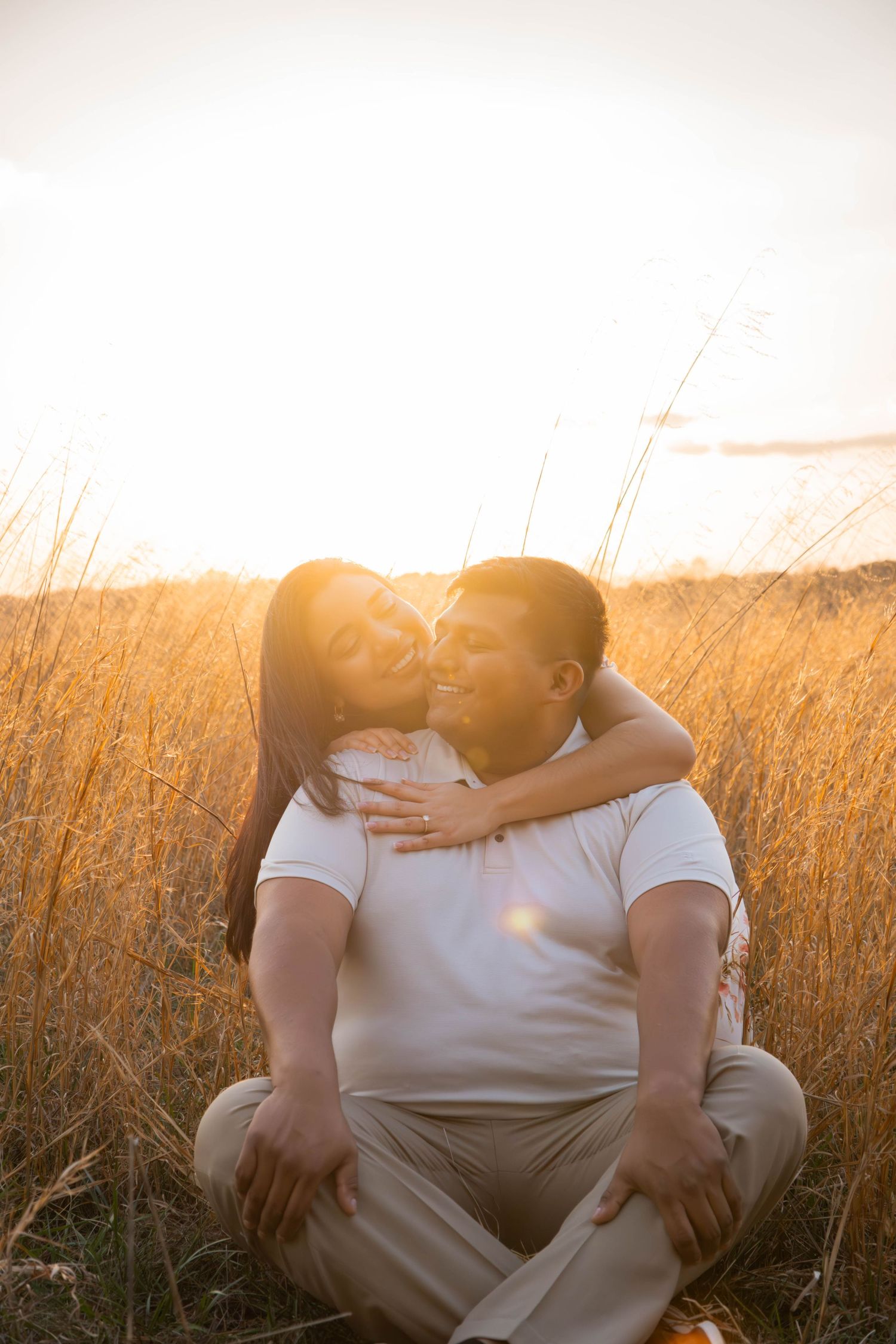 A romantic couple embraces in a golden wheat field at sunset casting a warm silhouette against the glowing sky.