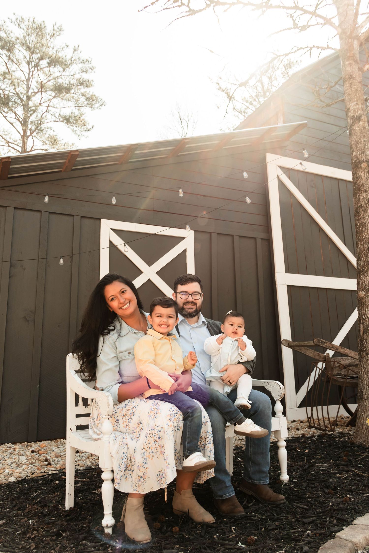 Sunlit family photo against rustic barn backdrop with white trim details.