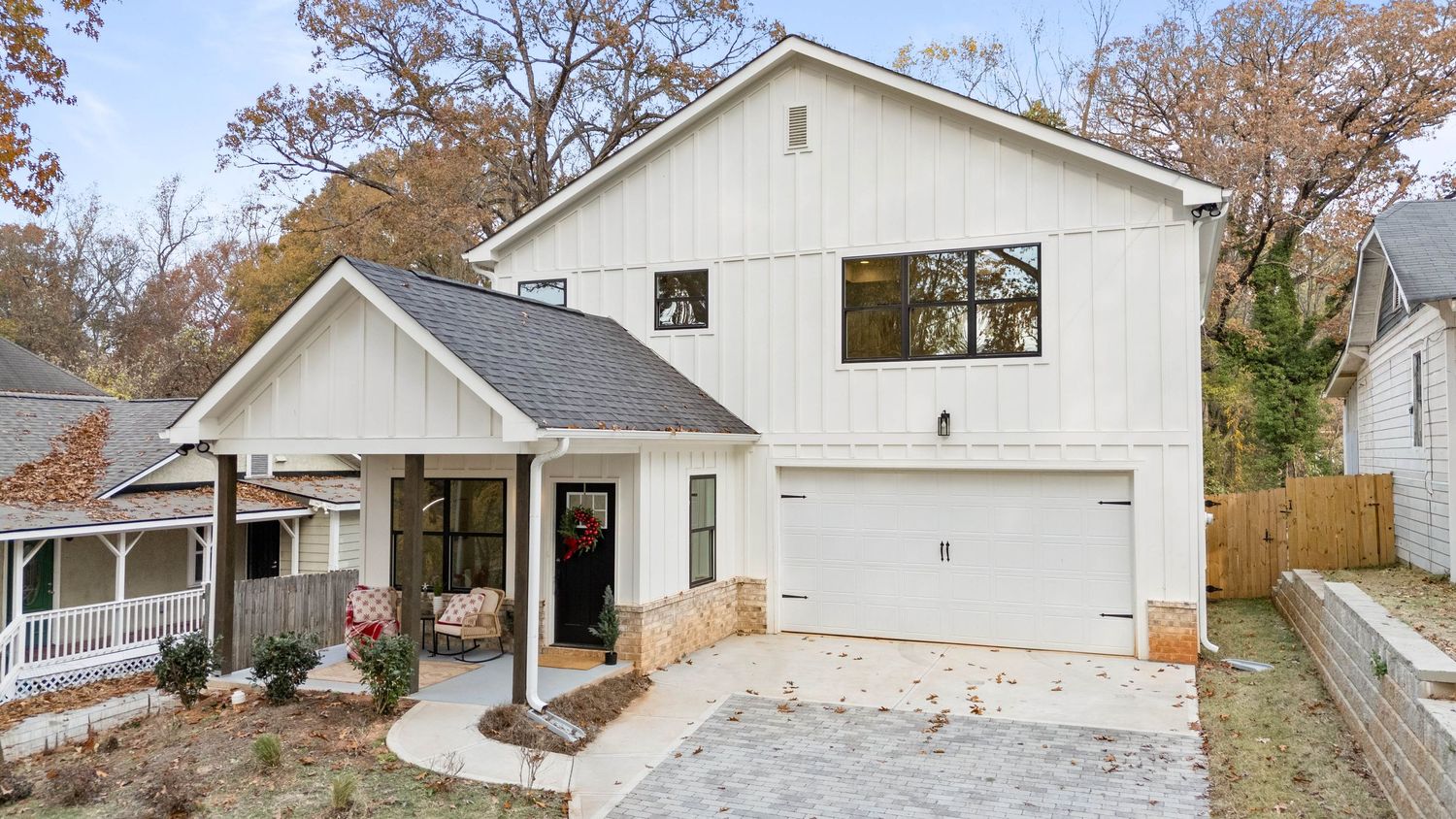 Panoramic view of a white residential house exterior with autumn trees and attached garage in suburban neighborhood.