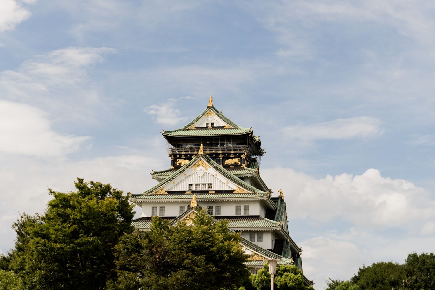 Traditional Japanese castle architecture with white walls and ornate green roof details against blue sky.
