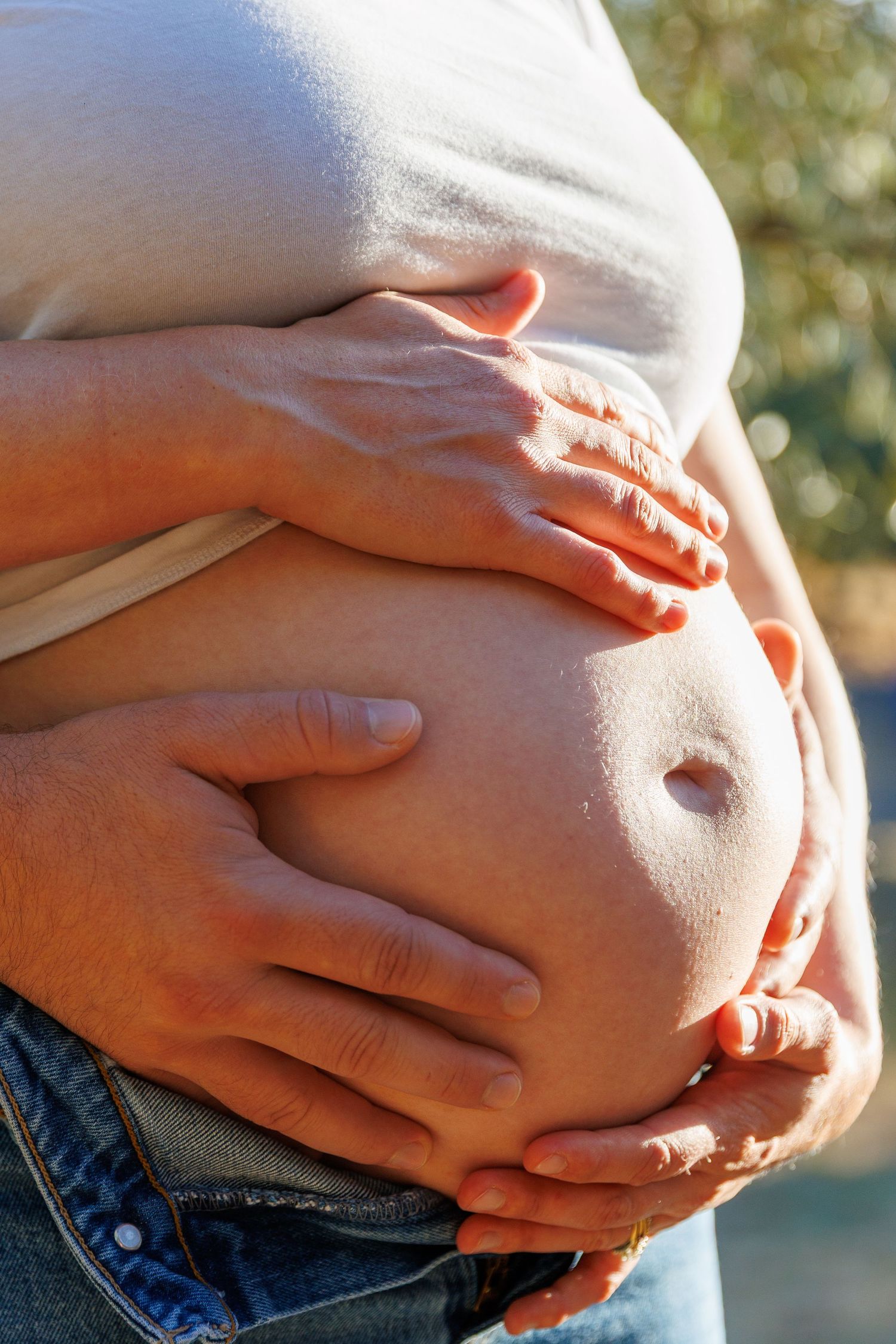 Close-up of Lily’s belly with both her and Travis’s hands gently holding her baby bump together.