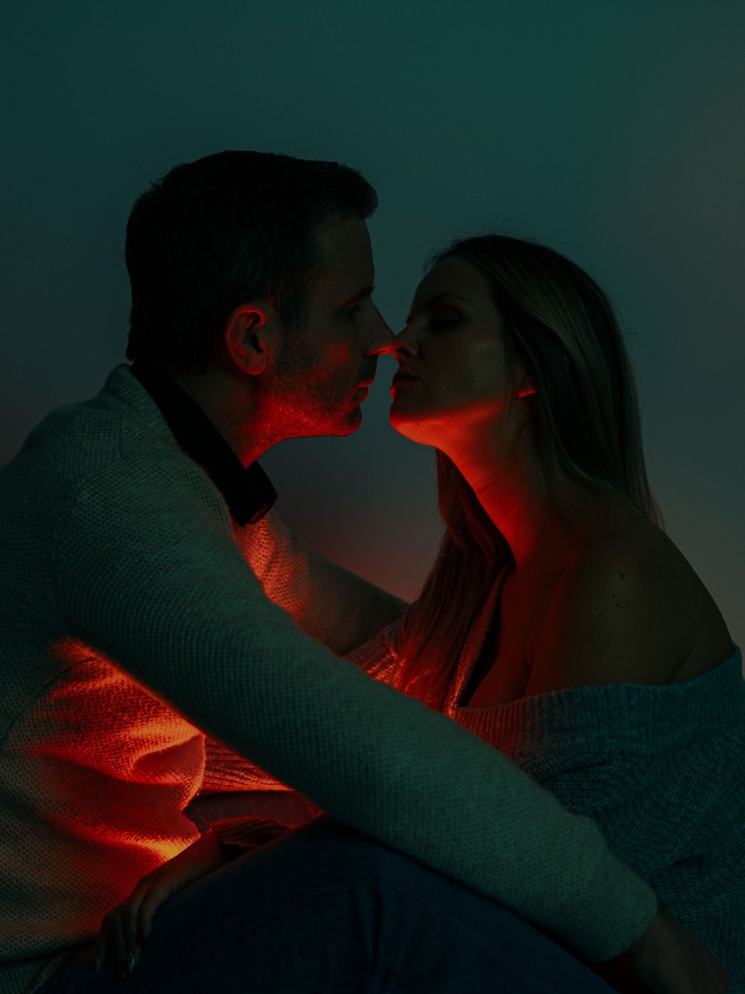Romantic couple in silhouette illuminated by dramatic red lighting against a dark teal background.