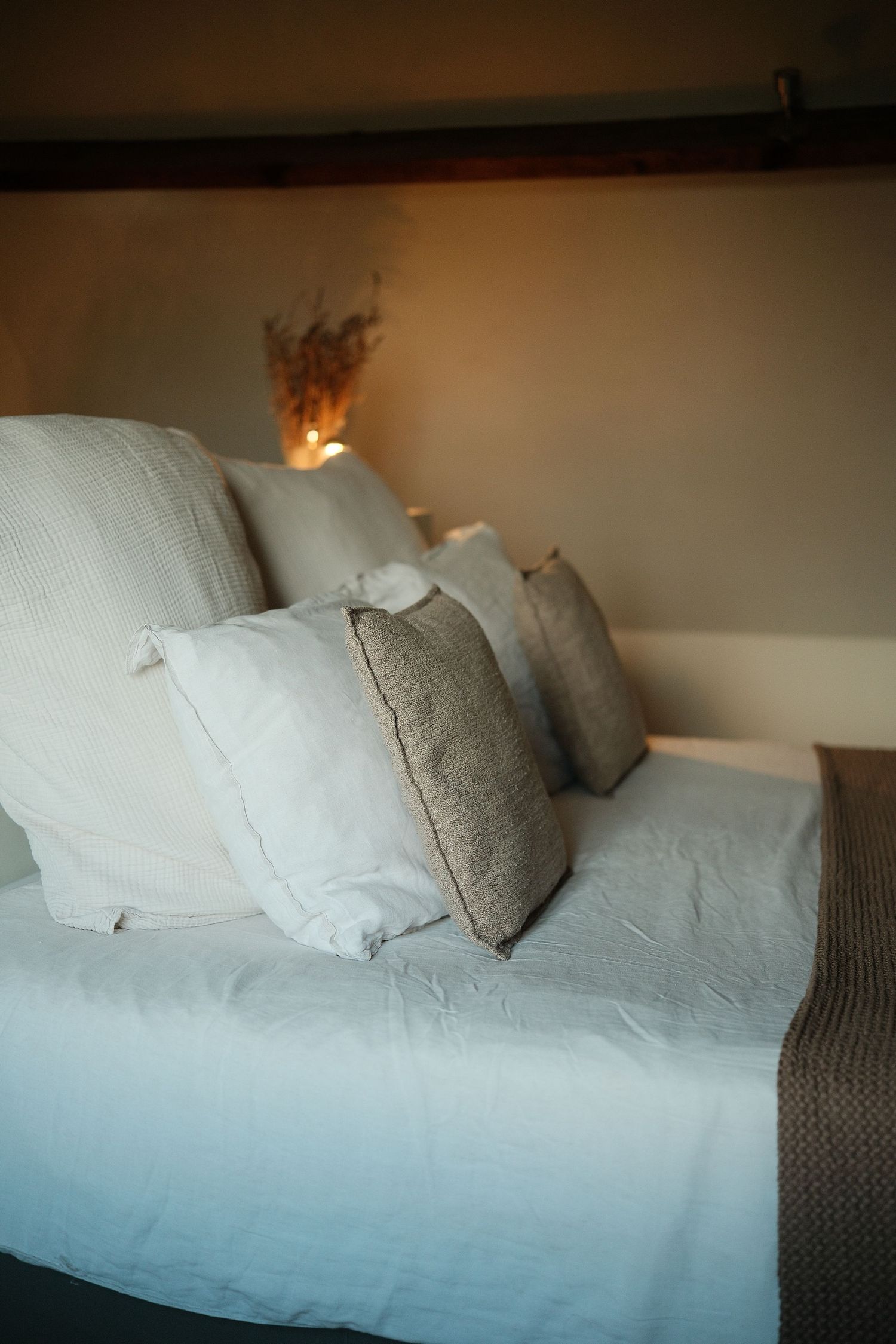 Comfortable bed with gray and white pillows in warm ambient lighting.