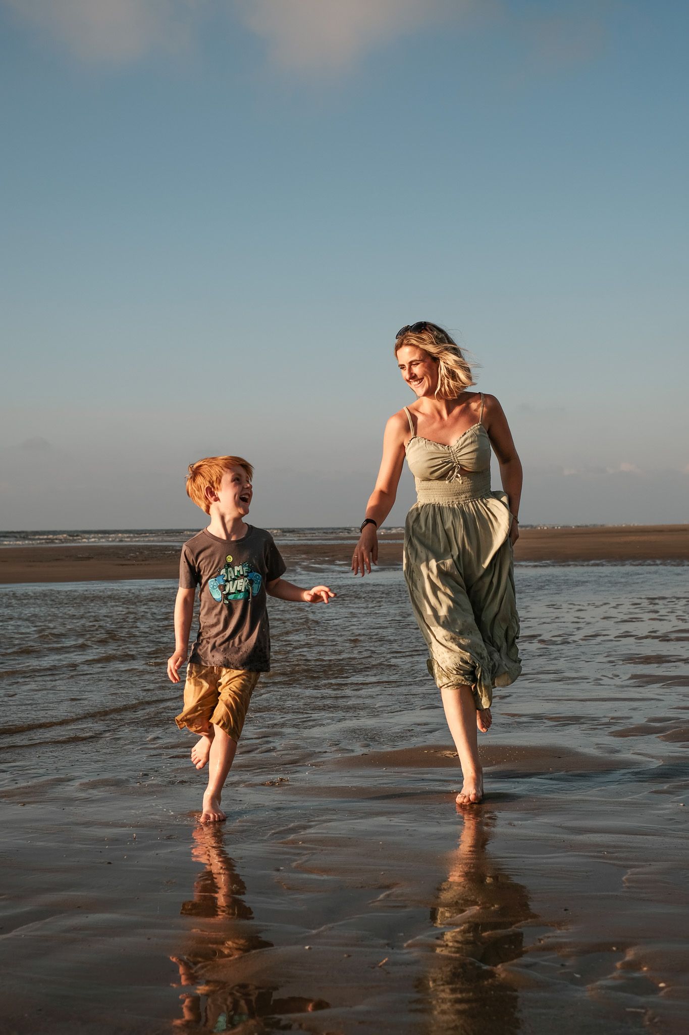 Playful beach scene with figures splashing through shallow water at sunset.