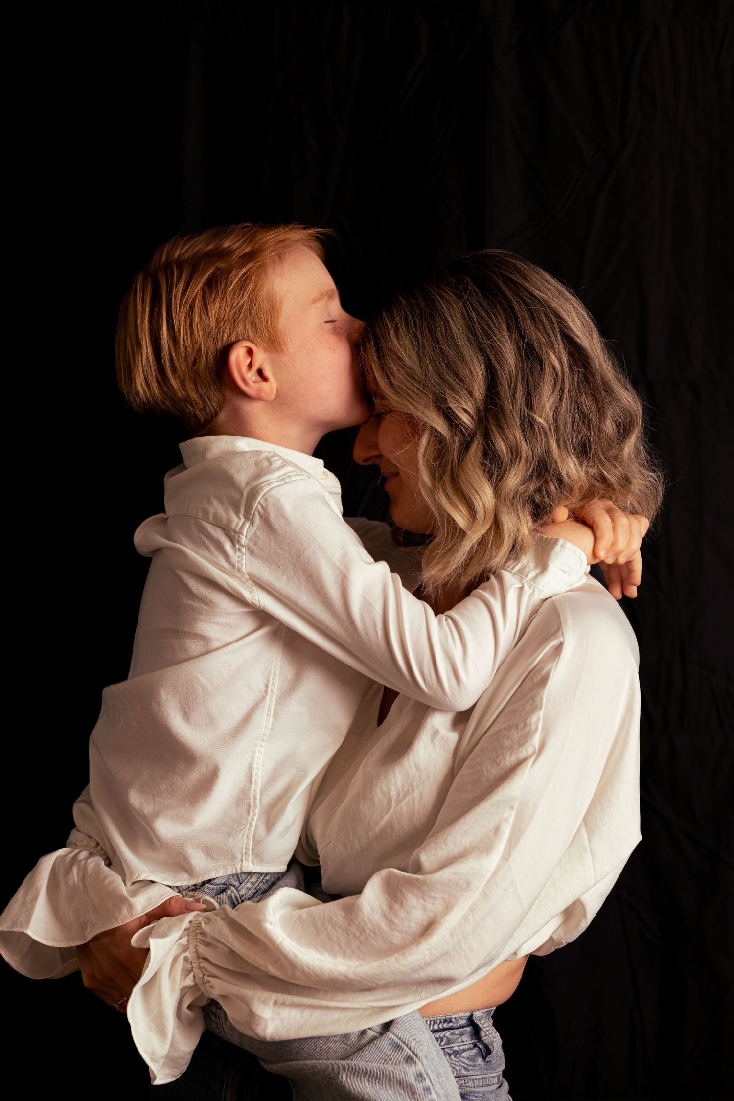 Intimate portrait of two people in white shirts embracing against black background.