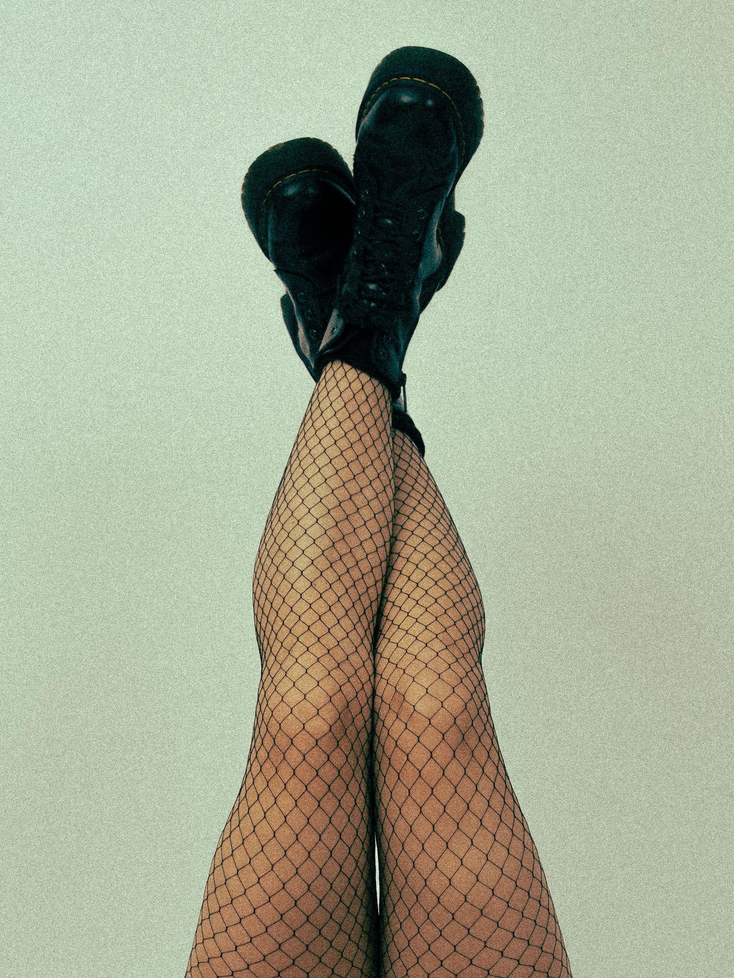 Close-up of legs wearing black fishnet stockings against a mint green background.