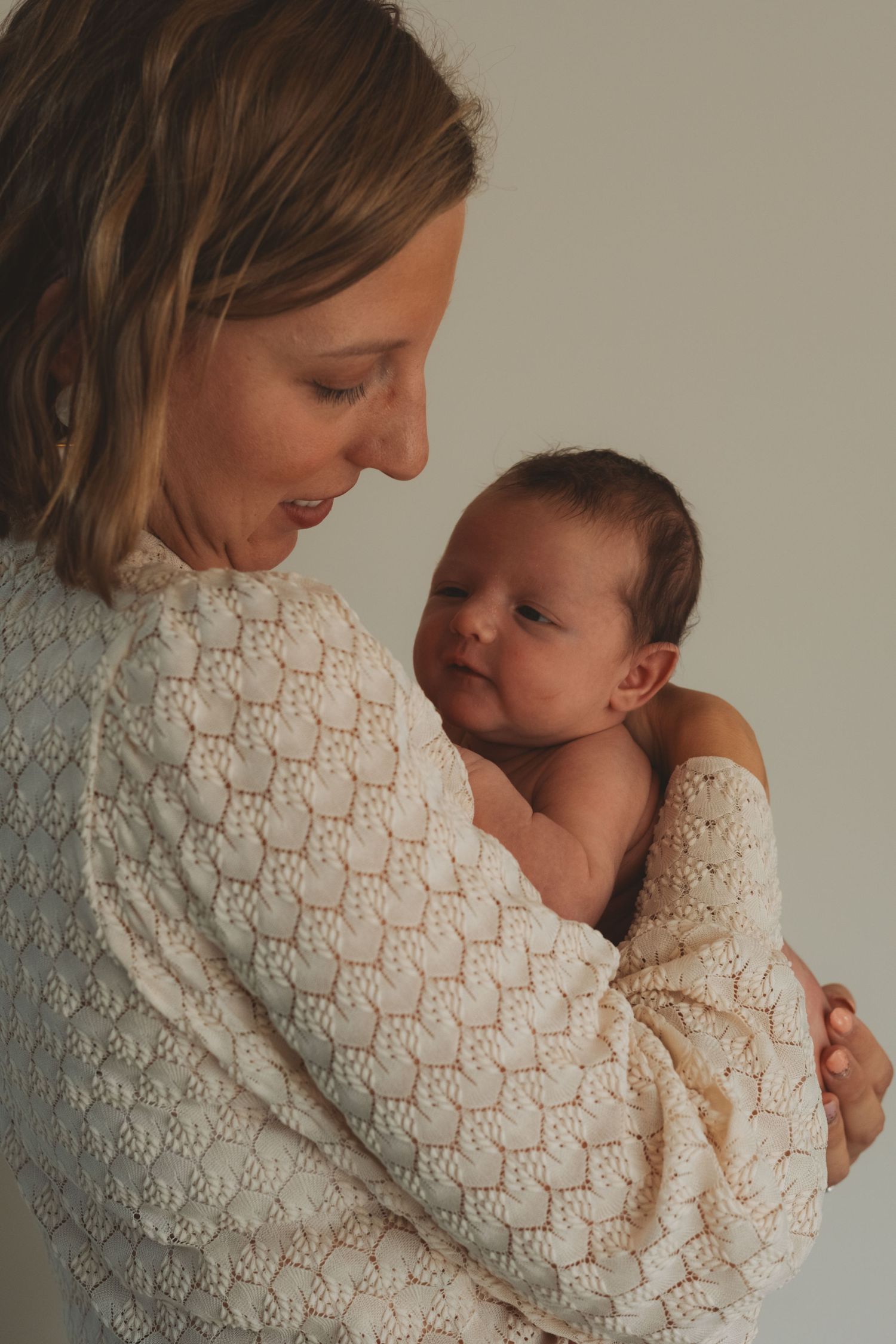 A tender moment between parent and newborn baby captured in a series of intimate portraits against a neutral background.