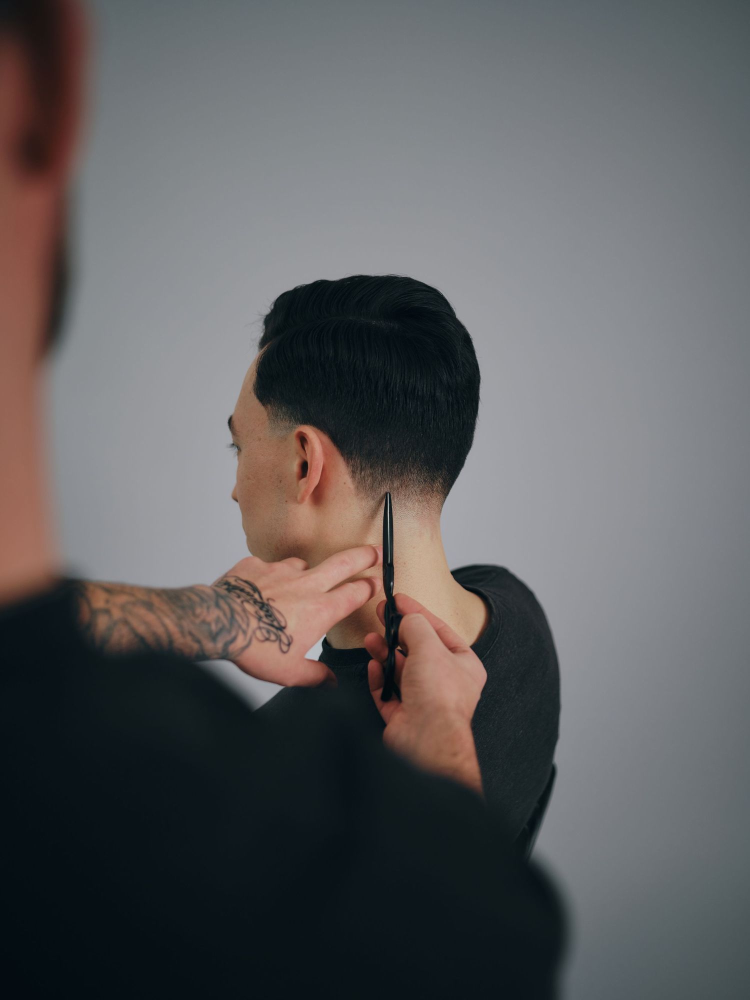 Tattooed barber using scissors to trim hair at neckline during a precise haircut service.