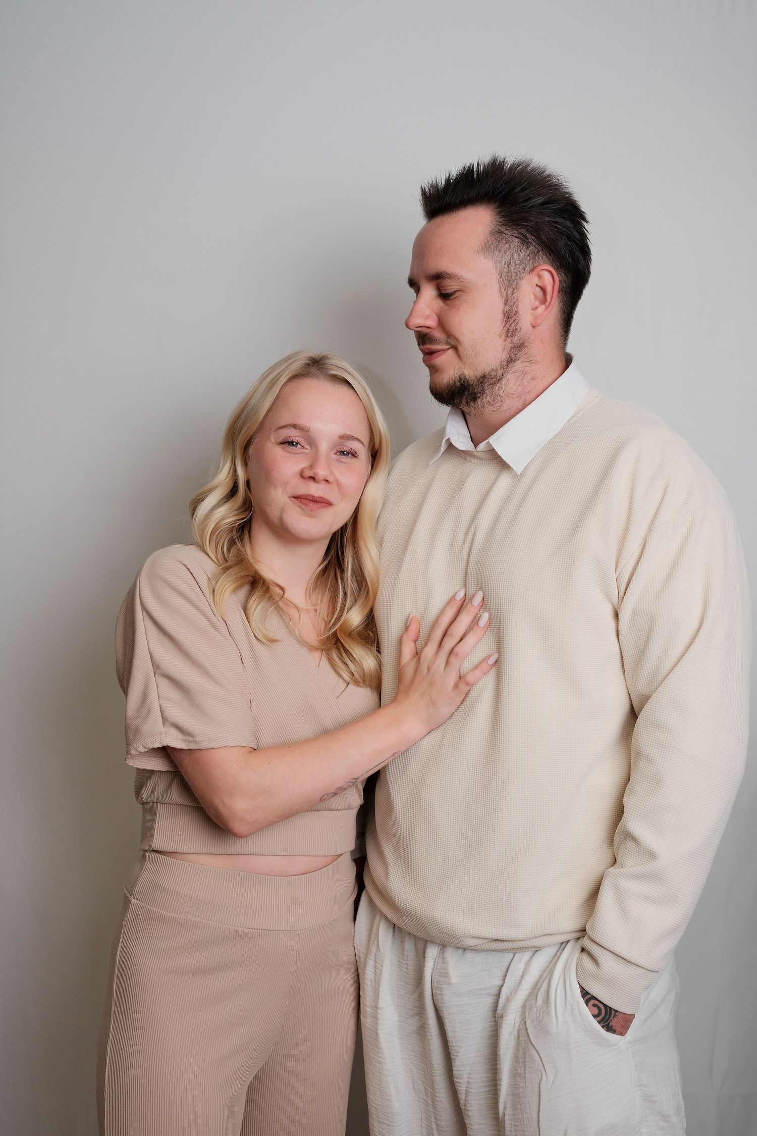 Couple in neutral colored clothing posing against grey background.
